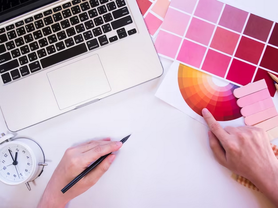 Image of a hand gripping a pen, alongside a colorful palette and a laptop.